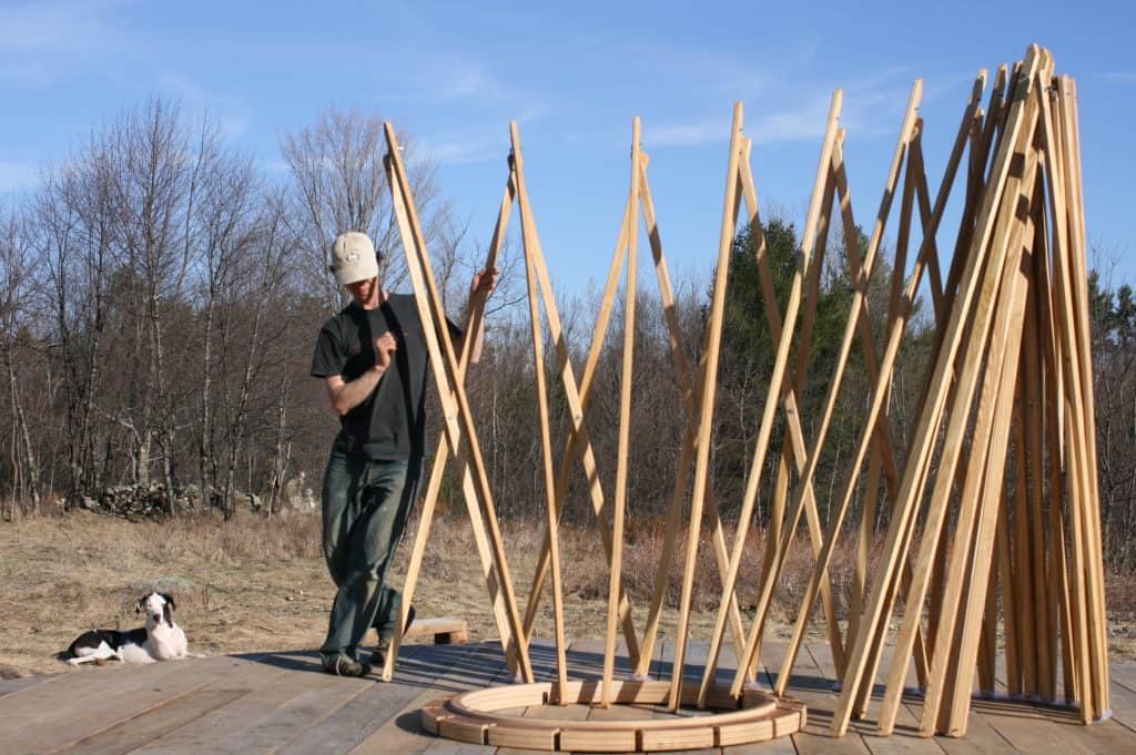 Portable, lightweight four-season Canadian yurt frame, being assembled outdoors with wooden framework in natural setting
