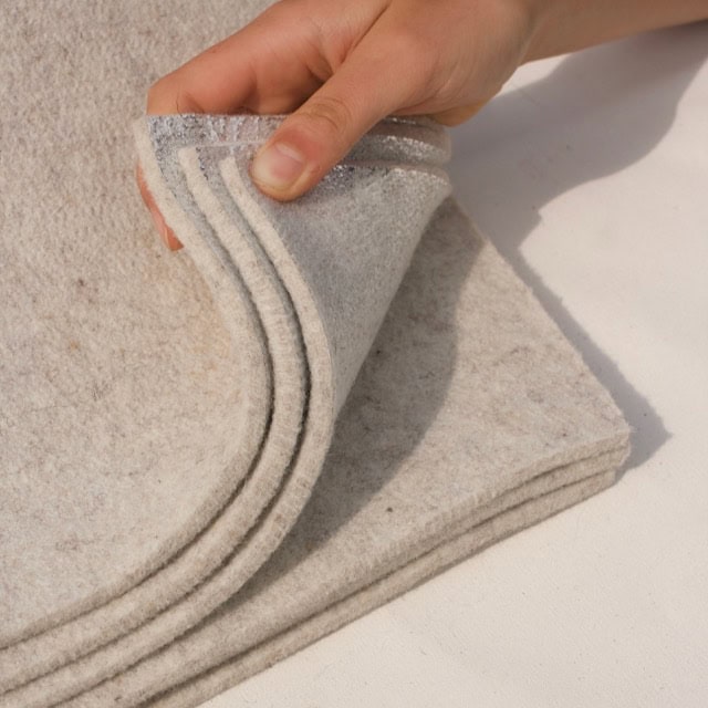 Hand holding thick layers of non-toxic radiant wool felt insulation engineered for 4-season yurts.